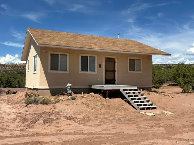 Stucco exterior with a brown shingle roof, elevated wood porch, and multi-paned windows