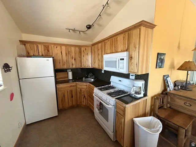 Kitchen featuring wood-finish cabinetry, dark countertops, white appliances, and track lighting