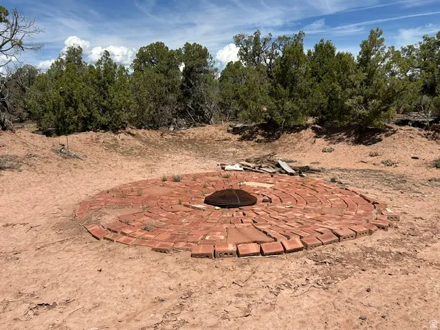 Circular brick feature with a central metal grate, surrounded by natural terrain and evergreen trees