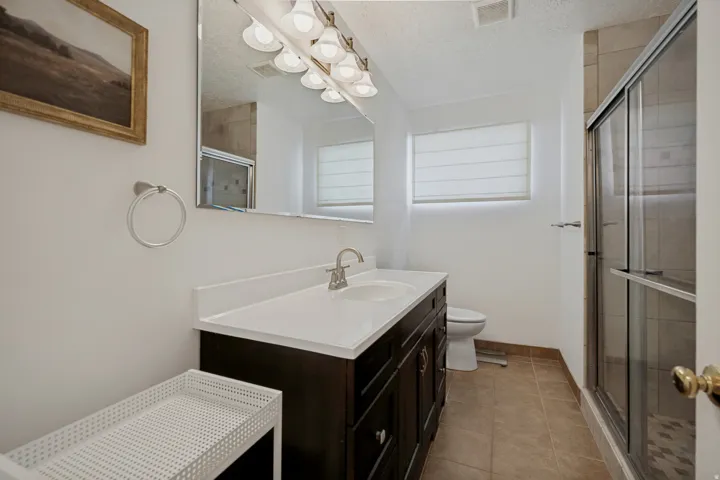 Dark wood-finish vanity with a white countertop and integrated sink, framed mirror, and glass-enclosed shower with tile surround