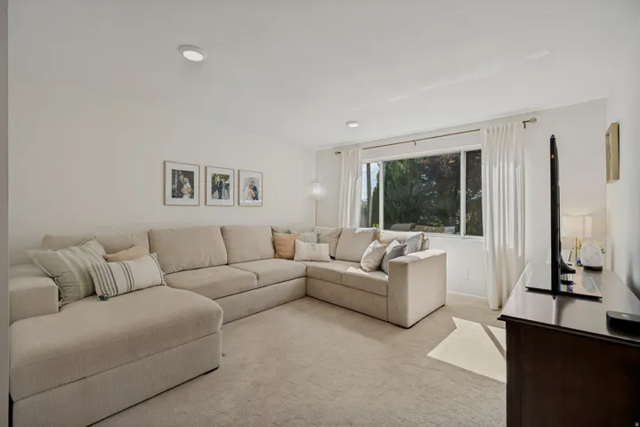 Recessed ceiling lighting, broad window, light-toned carpeting, and a dark wood-finish media console