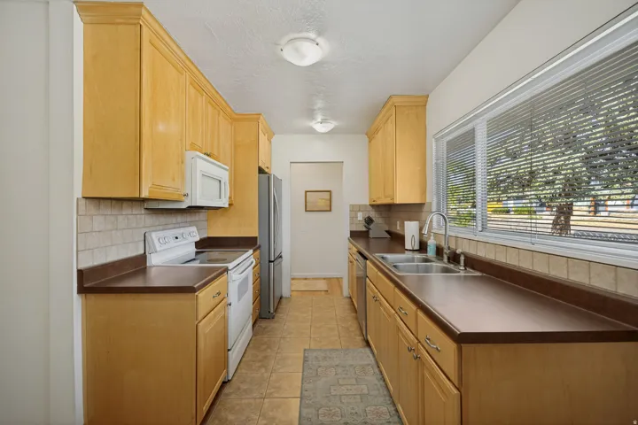 Galley kitchen featuring wood cabinetry, solid surface countertops, tile flooring, and a stainless steel double basin sink