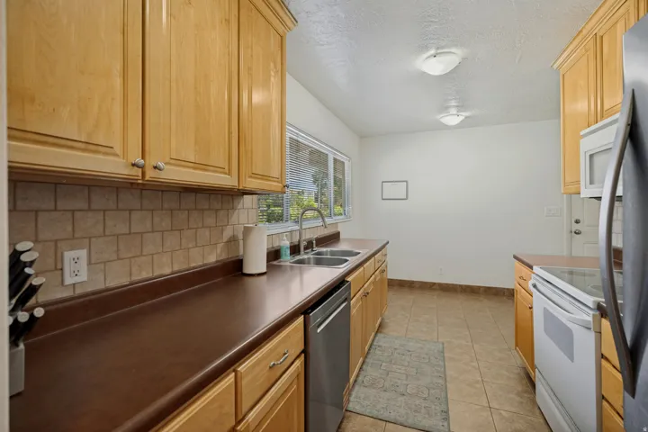 Kitchen featuring wood cabinetry, a dual basin stainless steel sink, a tile backsplash, and tile flooring