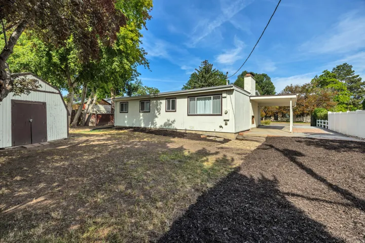 Exterior property featuring a detached shed, paved driveway, carport, and mature trees