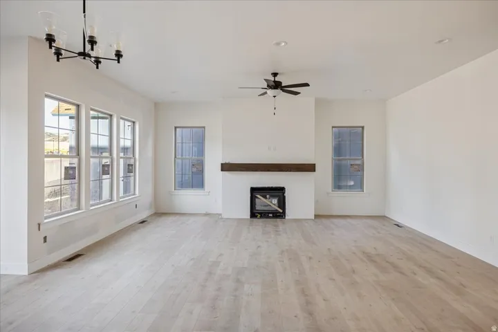 Spacious great room showcasing wide-plank wood-finish flooring, abundant natural light from triple French doors and dual windows, ceiling fan with pendant lighting, and a fireplace with wood mantel surround