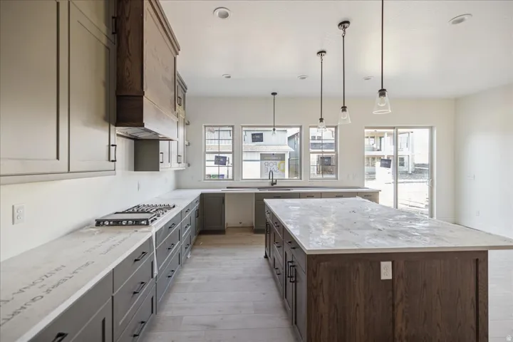 Spacious kitchen featuring an expansive central island with a stone countertop, a gas cooktop, and a sliding glass door for outdoor access