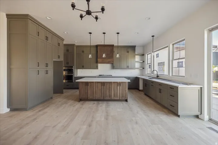 Spacious kitchen featuring extensive cabinetry, a large wood-finish island with a light-toned countertop, double wall ovens, a built-in cooktop, and wood-finish flooring
