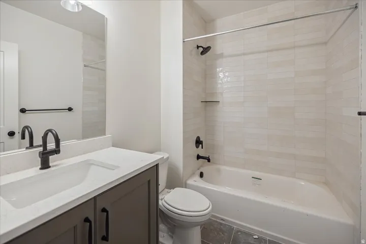 Bathroom featuring a dark wood-finish vanity, light-toned countertop, integrated sink, matte black fixtures, and subway-tiled shower surround