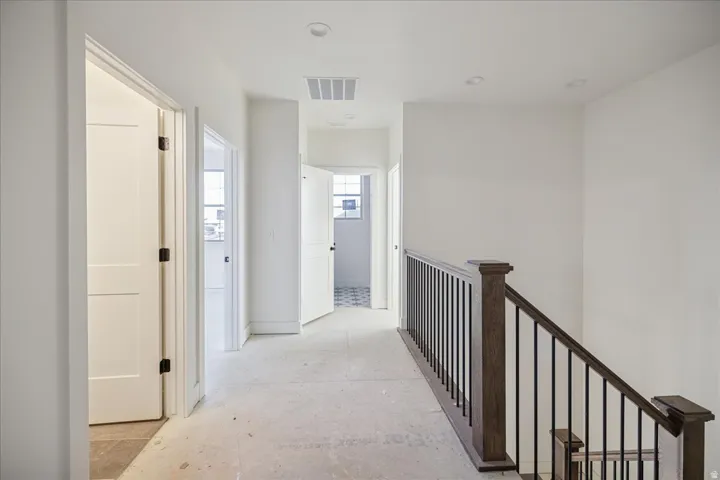 Hallway with recessed lighting, painted white walls, wood-finish stair railing with black balusters, and paneled interior doors