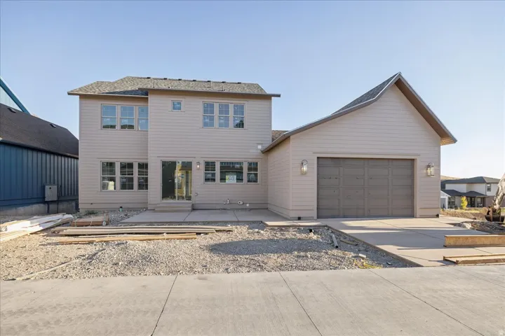Two-story exterior with light-colored siding, a two-car garage with a gray door, multiple windows, and a sliding glass door
