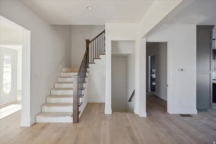 Wood-finish flooring throughout, staircase with dark wood handrail and wrought iron spindles, recessed lighting, white trim and wall paint, and a built-in dark cabinetry system