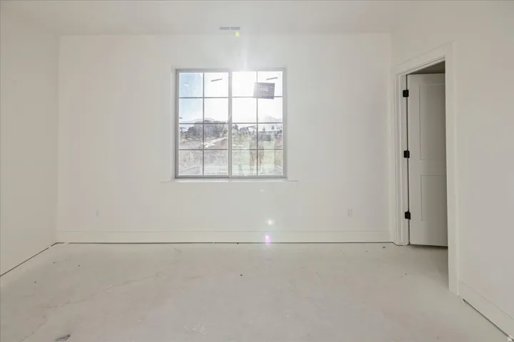 Spacious room featuring a grid-pattern window, white painted walls, a panel door with dark hardware, and concrete flooring
