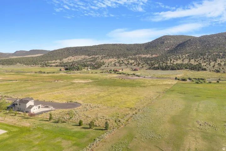 Expansive land parcel featuring a contemporary residence, paved circular driveway, and mountainous backdrop