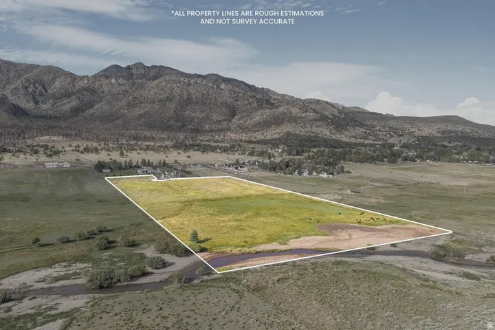 Expansive land parcel featuring open fields, a natural stream, and distant mountainous terrain