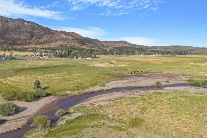Expansive landscape featuring a meandering waterway, verdant fields, distant mountain range, and a cluster of residences