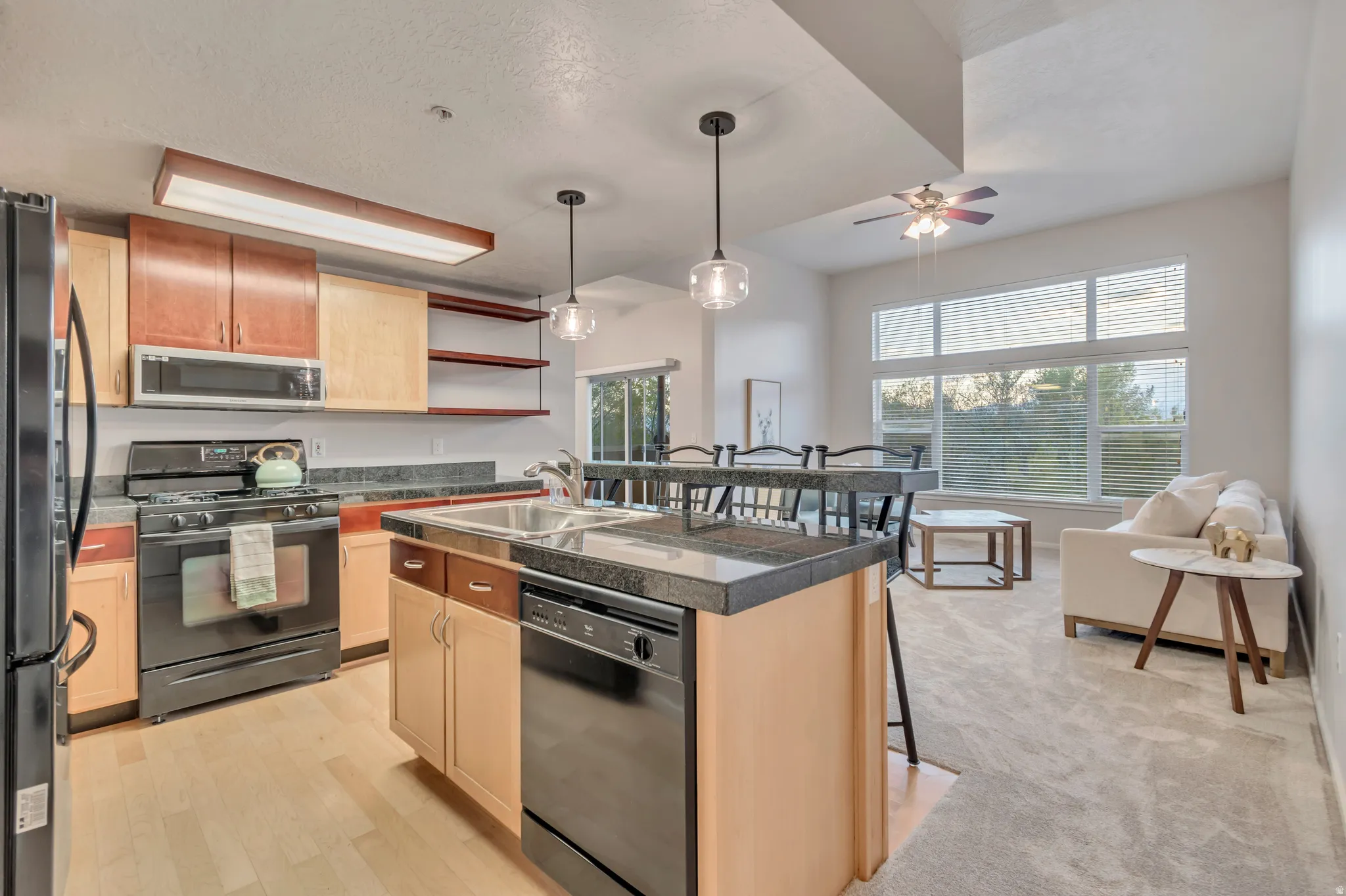 Open-concept living space with a kitchen island, black appliances, wood-finish flooring, and expansive windows