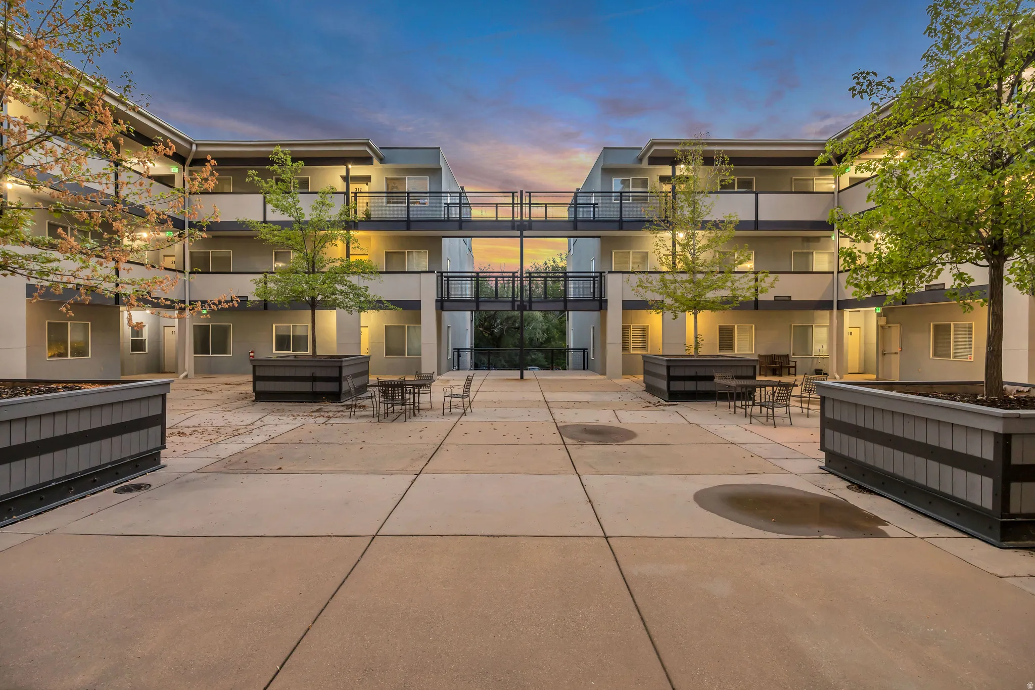 Central courtyard with concrete paving, multiple levels of balconies with dark railings, and built-in planters with trees
