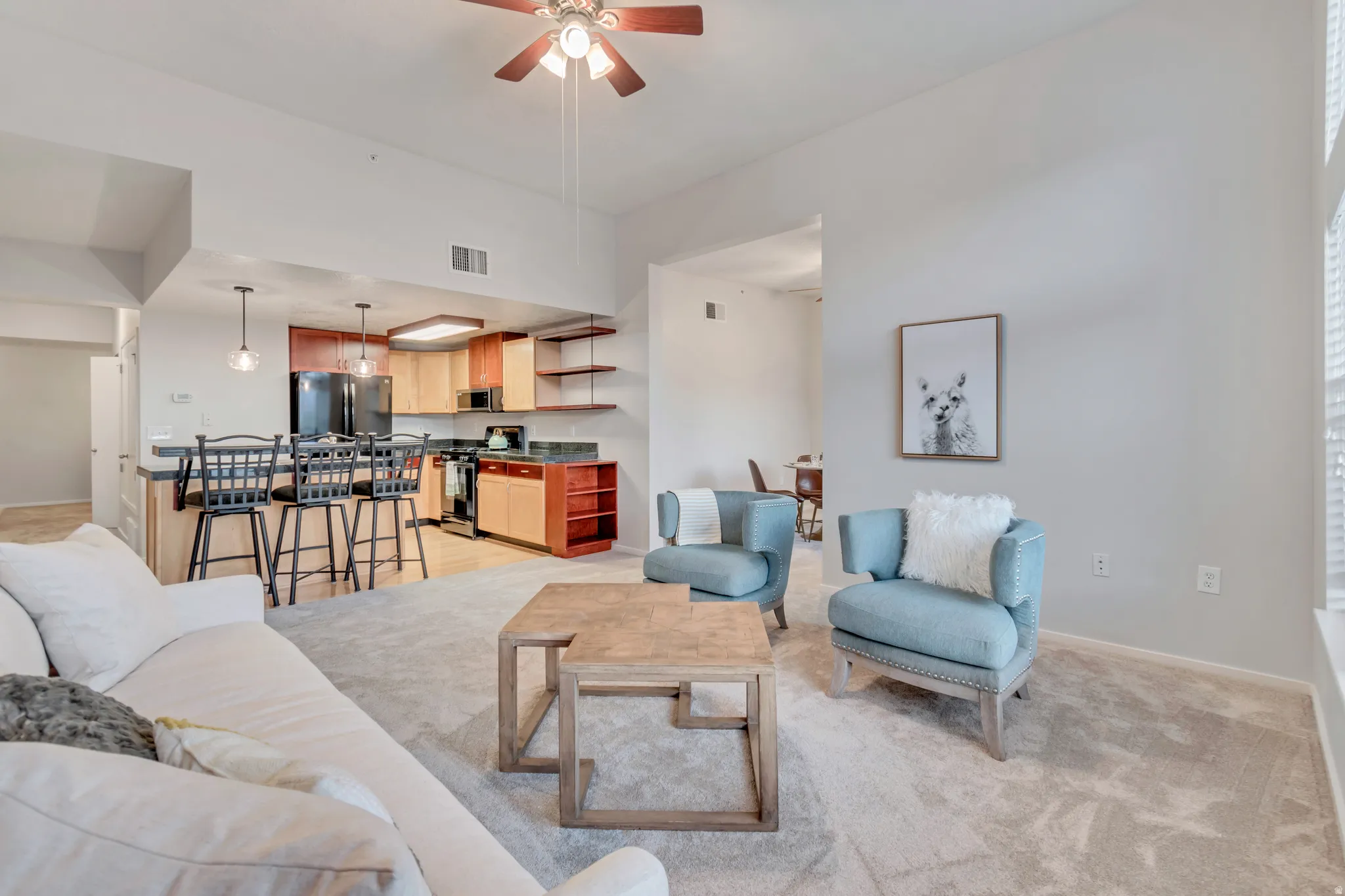 Open-concept living space with light neutral wall tones, vaulted ceiling, and carpet flooring