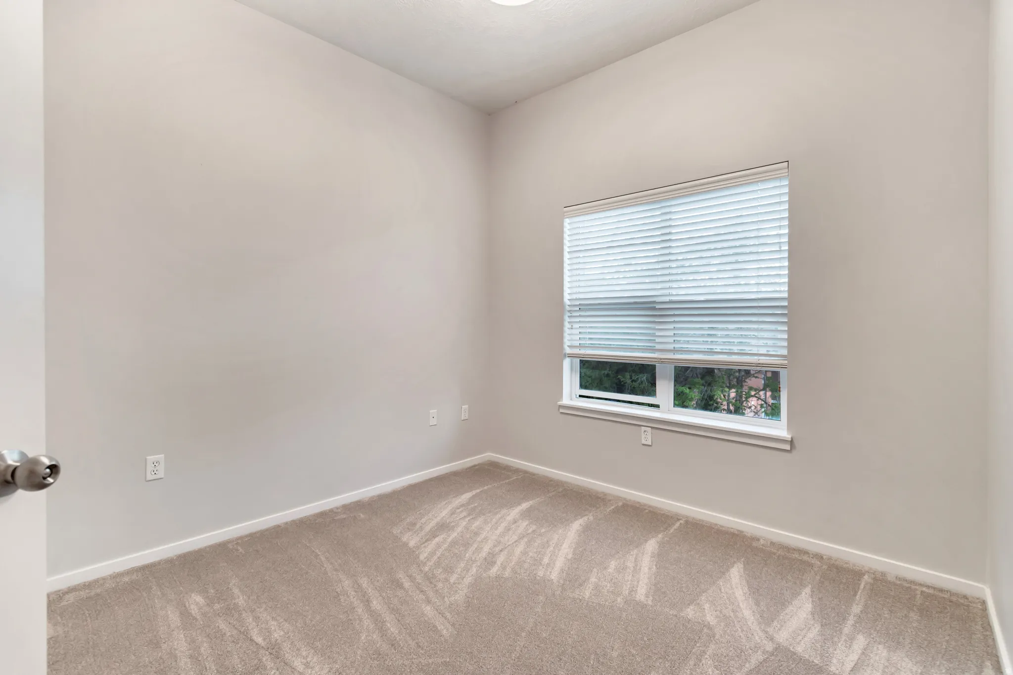 Light gray walls with a single window, white trim, and light-colored carpeting
