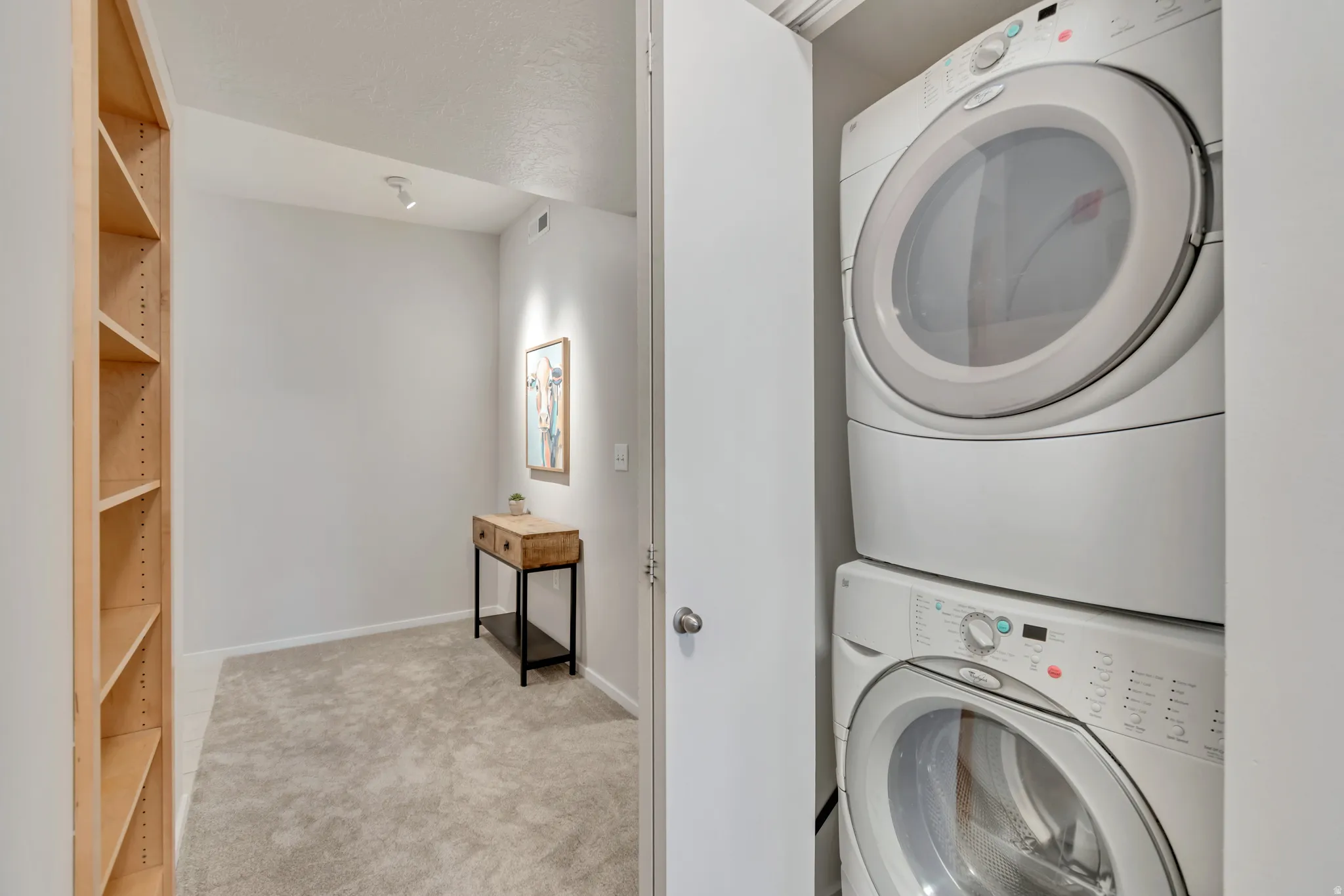 Built-in shelving, recessed lighting, and soft gray carpeting, with a stacked washer and dryer unit