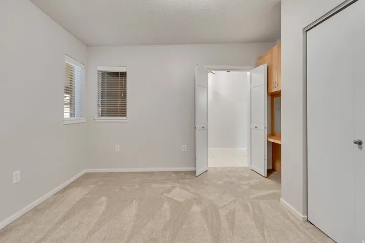 Neutral-toned carpeting, dual windows with blinds, and built-in wood cabinetry