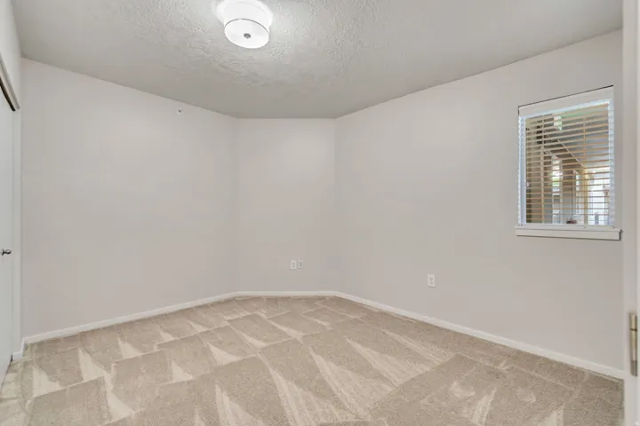 Neutral tone wall finish, textured ceiling, flush mount ceiling light fixture, window with blinds, and patterned carpeting