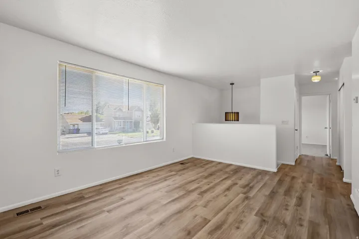Wood-finish flooring throughout, large window with blinds, modern pendant light fixture, white walls, and a consistent ceiling finish