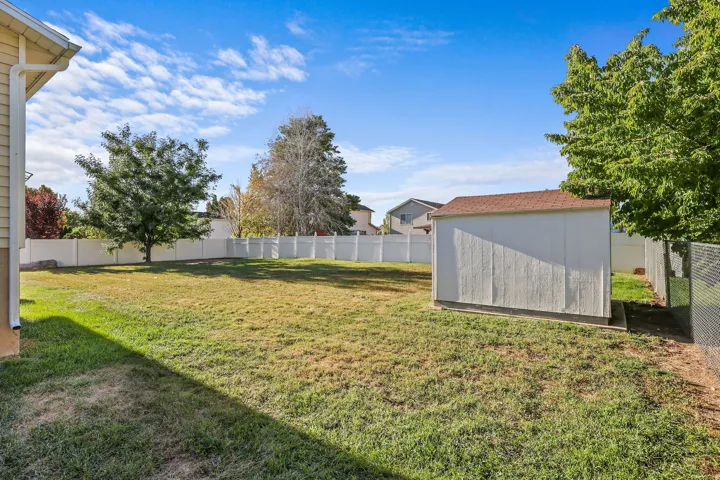 Expansive backyard featuring a manicured lawn, white vinyl fencing, and a dedicated storage shed