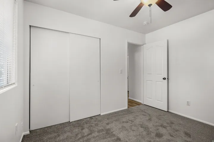 Neutral wall finishes with a ceiling fan, carpet flooring, a white paneled door, and sliding closet doors
