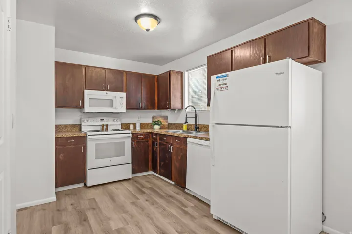 Kitchen featuring wood-finish cabinetry, light-toned countertops, white appliances, and wood-finish flooring