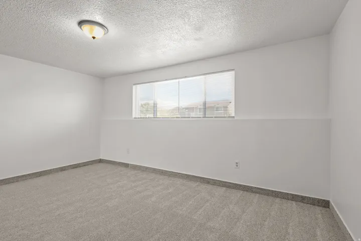 Recessed window with blinds, overhead lighting, textured ceiling, and gray carpet flooring