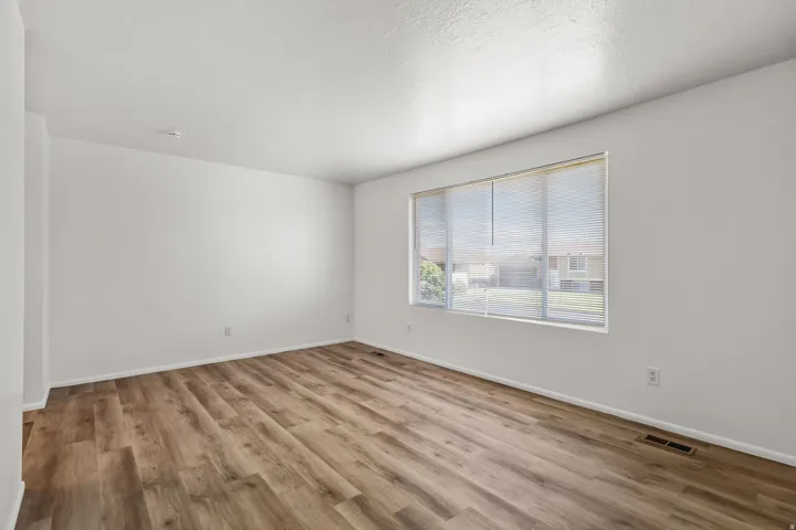 Spacious room featuring wood-finish flooring, white walls, and a large window with blinds