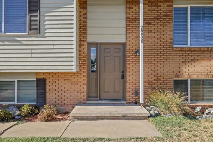 Brick and siding exterior, concrete entryway, panel front door with sidelight, exterior wall sconce, and multiple windows