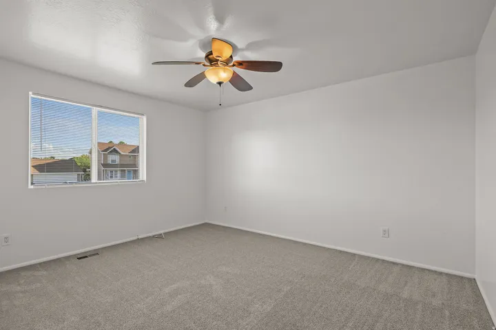 Carpeted room featuring a ceiling fan with light fixture and a window with blinds