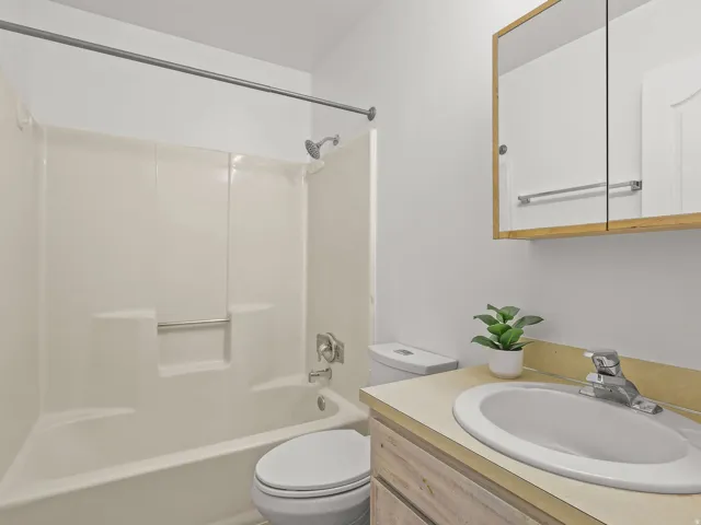 Clean and functional bathroom featuring a ceramic sink with chrome faucet, wood-finish vanity with integrated countertop storage, and an enclosed shower-tub combination with glass enclosure and chrome fixtures