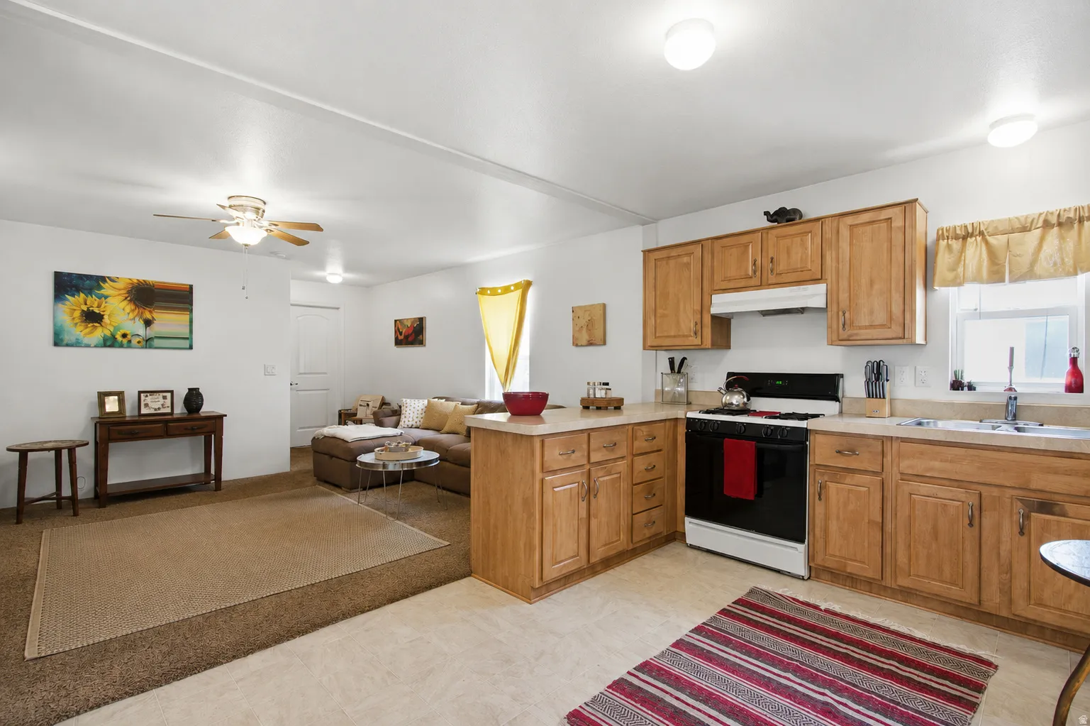 Open-concept living space featuring wood-finish cabinetry, a ceiling fan, and an integrated kitchen with a gas range