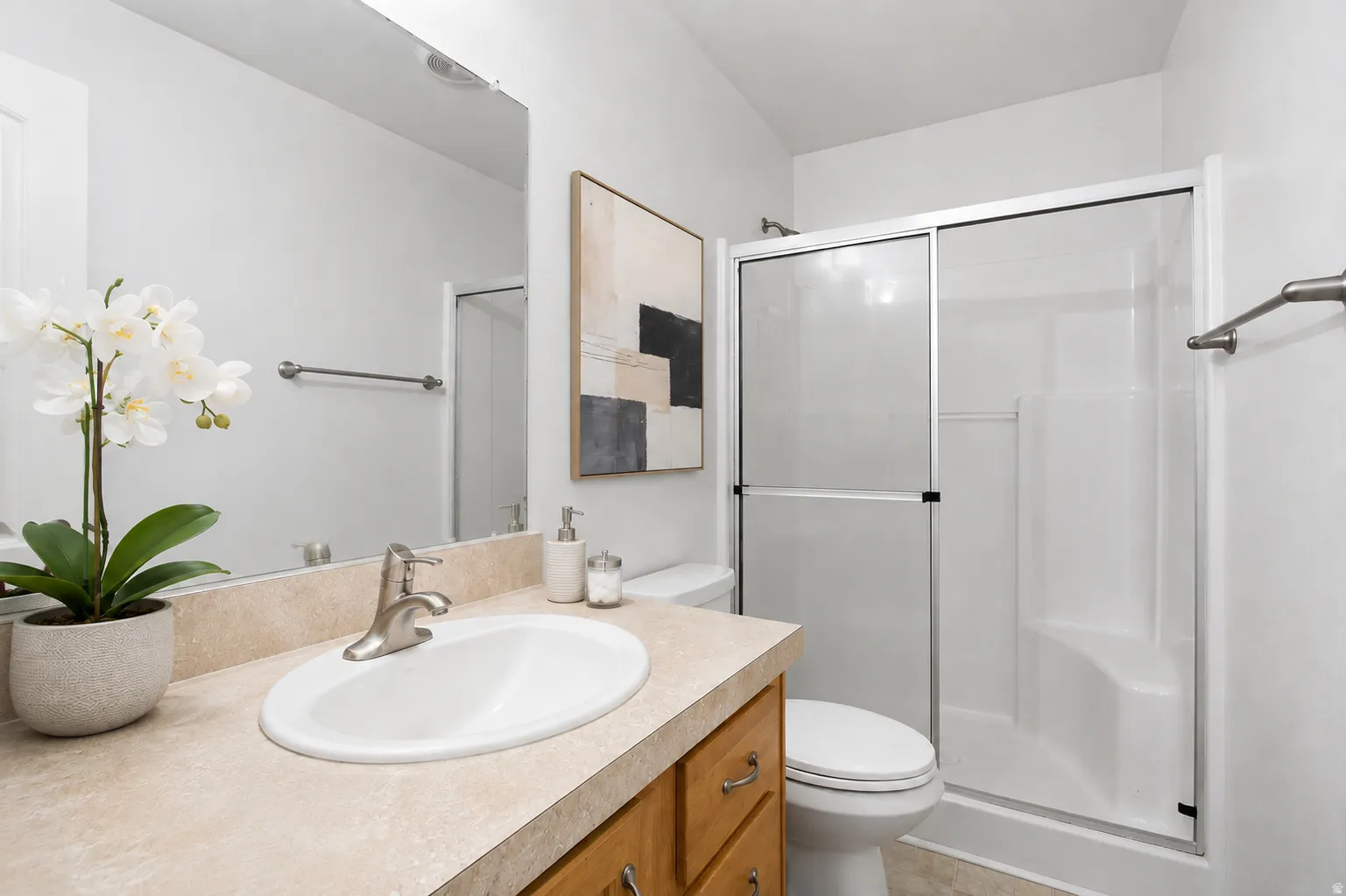 Bathroom featuring a light-toned countertop, wood-finish cabinetry with brushed nickel hardware, and a shower enclosure with sliding glass doors
