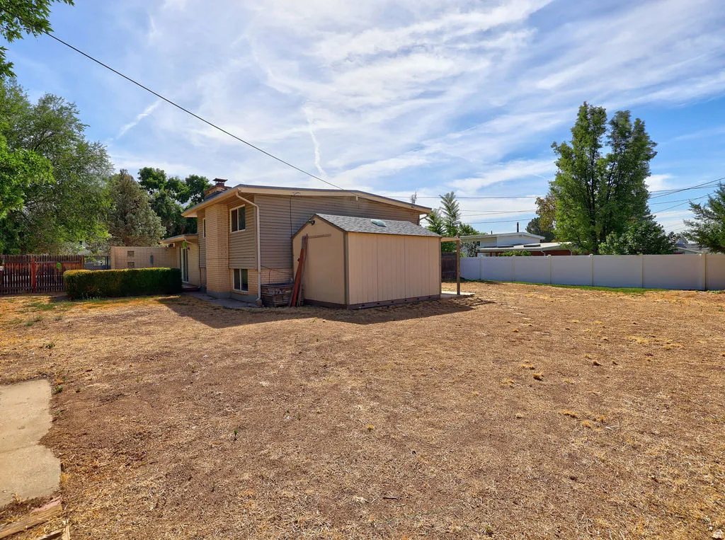Spacious backyard with a detached storage shed, privacy fencing, mature perimeter trees, and a ground-level patio