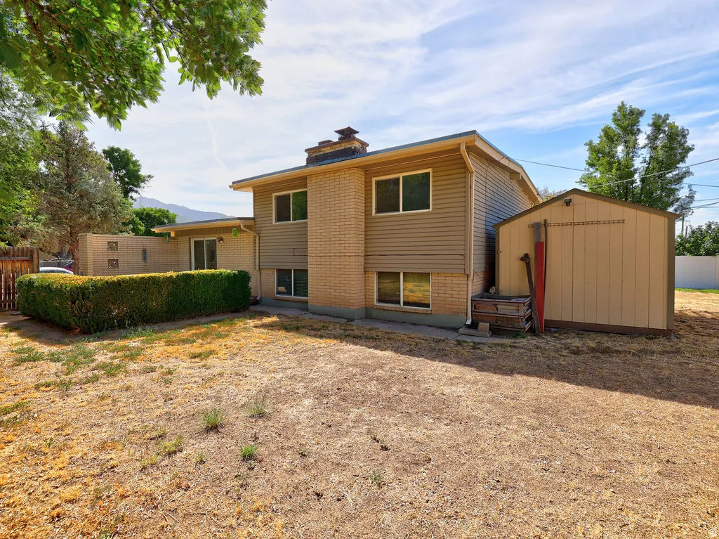 Rear exterior with a storage shed, a manicured hedge, and a sliding glass door