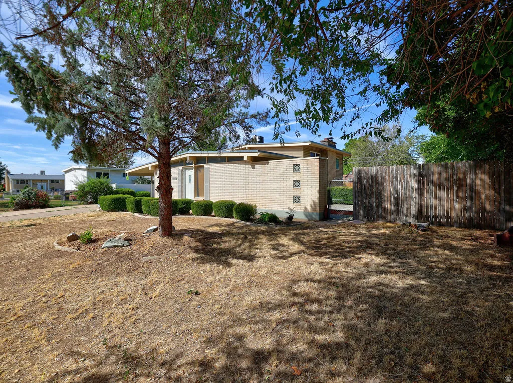 Exterior featuring a light brick facade, mature trees, and established perimeter fencing