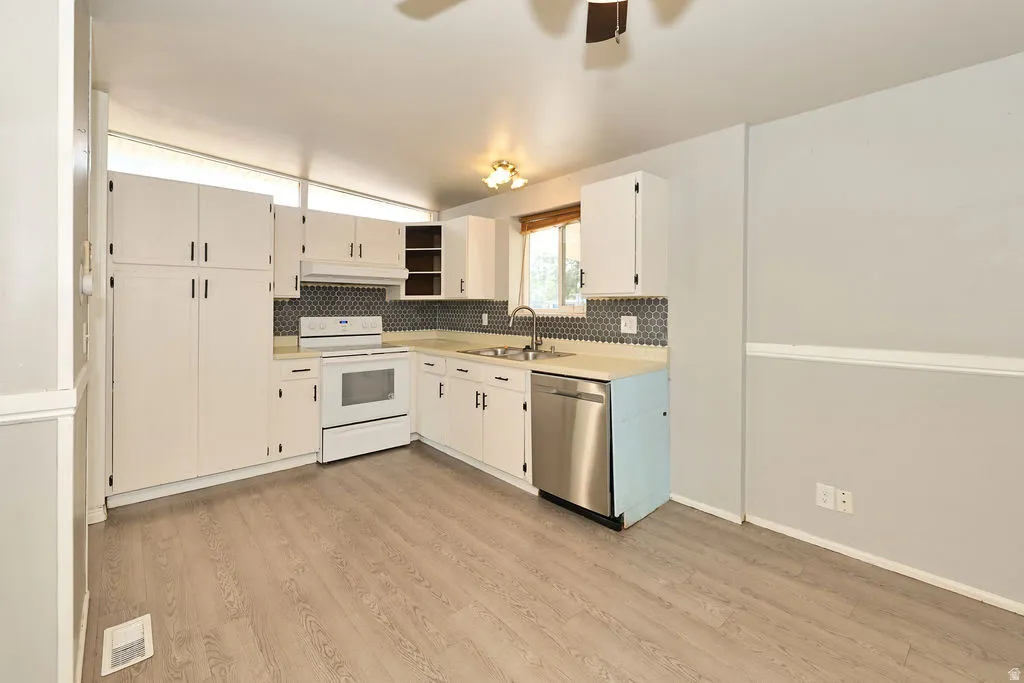 White cabinetry, wood-finish flooring, stainless steel dishwasher, tile backsplash, and overhead lighting fixture