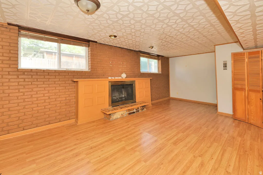 Wood-finish flooring, brick accent wall, fireplace with stone hearth, built-in wooden cabinetry, and patterned ceiling panels