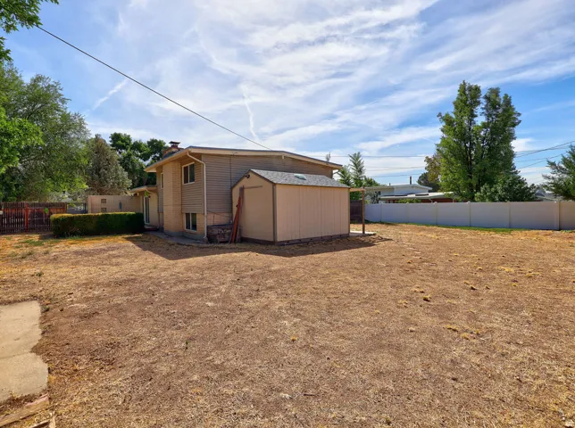 Spacious backyard with a detached storage shed, privacy fencing, mature perimeter trees, and a ground-level patio