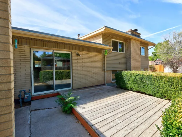 Expansive wood deck with a brick exterior, sliding glass doors, and mature hedge landscaping