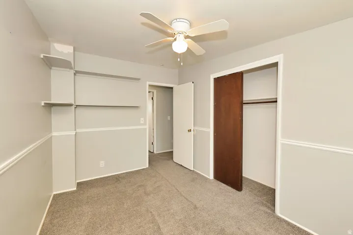 Wall-to-wall carpeting, ceiling fan with light fixture, built-in shelving, and a closet with a wood-finish sliding door