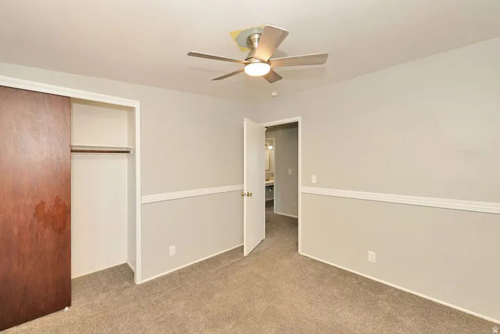 Carpeted room featuring a ceiling fan with integrated lighting, wood-finish sliding closet doors, and chair rail molding