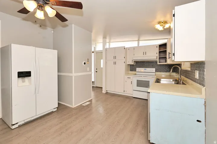 Wood-finish flooring, white cabinetry, integrated stainless steel sink, tiled backsplash, and ceiling fan