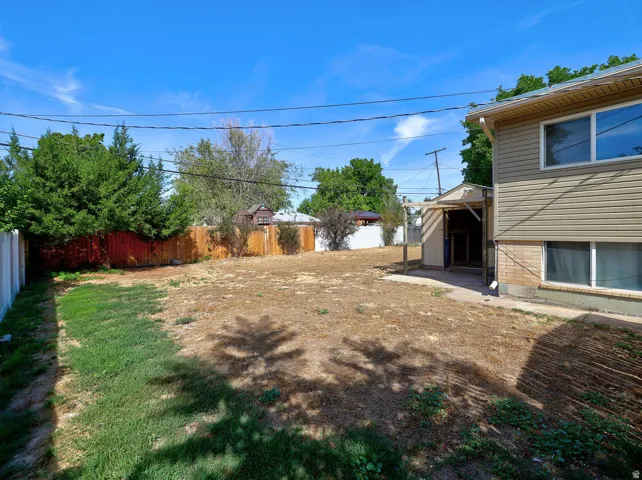 Expansive rear yard with a mix of natural ground cover and partial lawn, featuring a wood privacy fence and mature perimeter landscaping