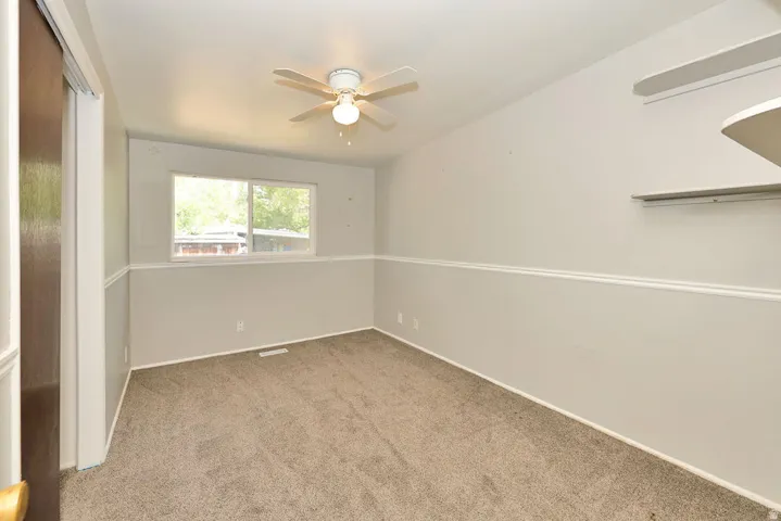 Carpeted room with a ceiling fan, dual windows, and built-in shelving