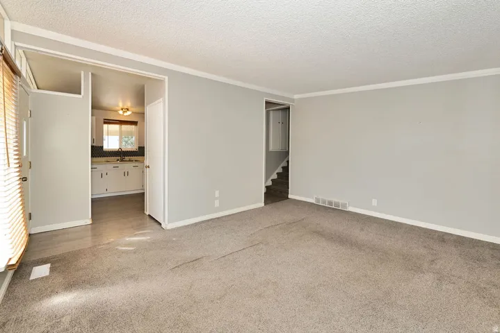 Neutral wall paint, crown molding, a built-in kitchen featuring white cabinetry and a backsplash, wood-finish flooring in the kitchen, and a staircase with a handrail
